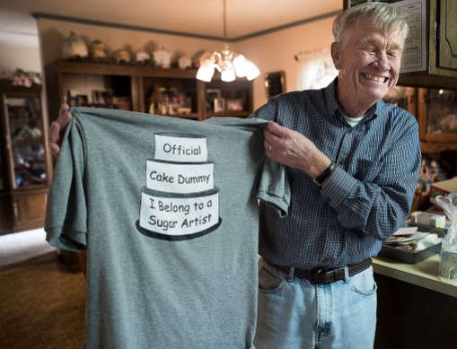 Clarence Miller laughs as he holds a shirt that says, "Official Cake Dummy. I Belong to a Sugar Artist." on March 27, 2018. (Photo by Rebecca Benson)