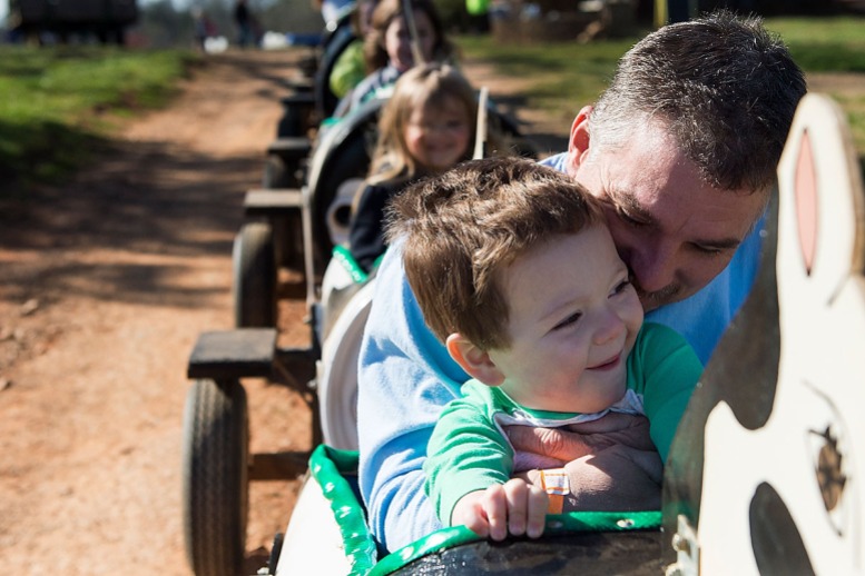 River Britt, 3, and his dad Joe Britt, ride the Cow Train at the Egg-cellent Adventure at Patterson Farm on March 31, 2018. (Photo by Rebecca Benson)